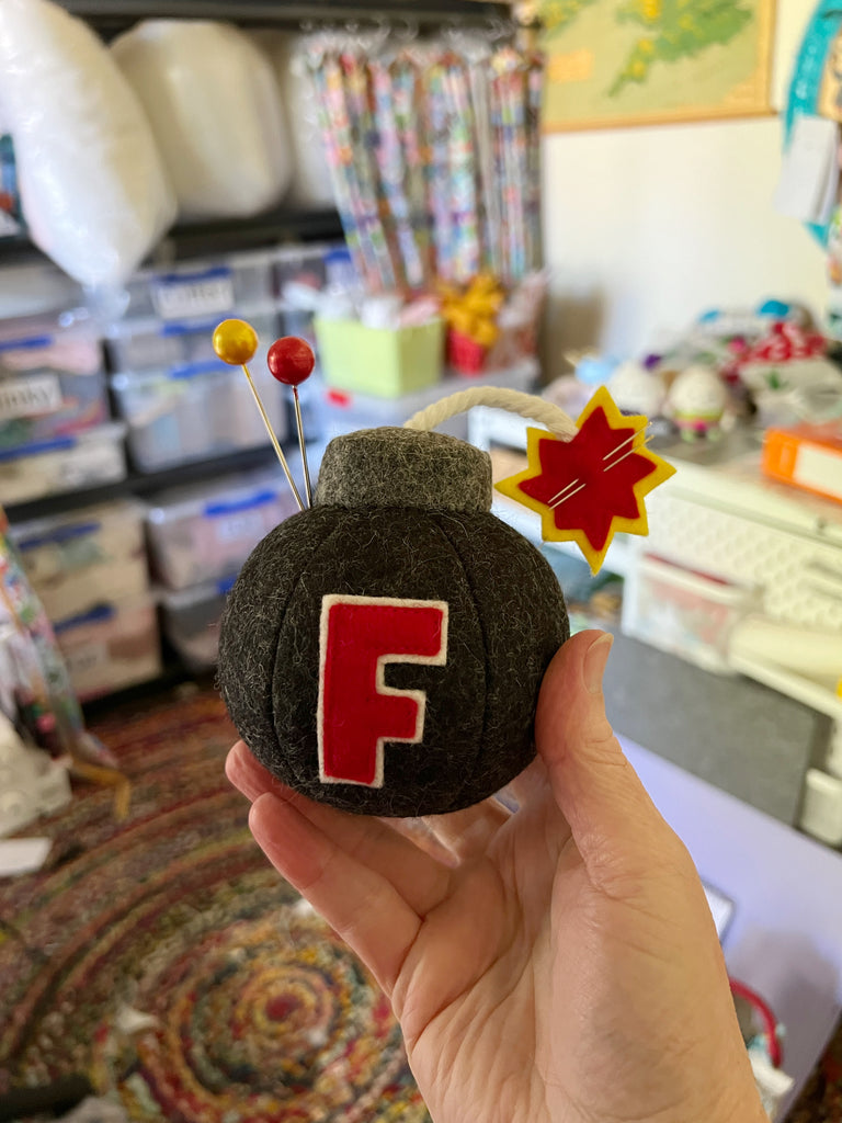 an F bomb pincushion being held in a sewing room
