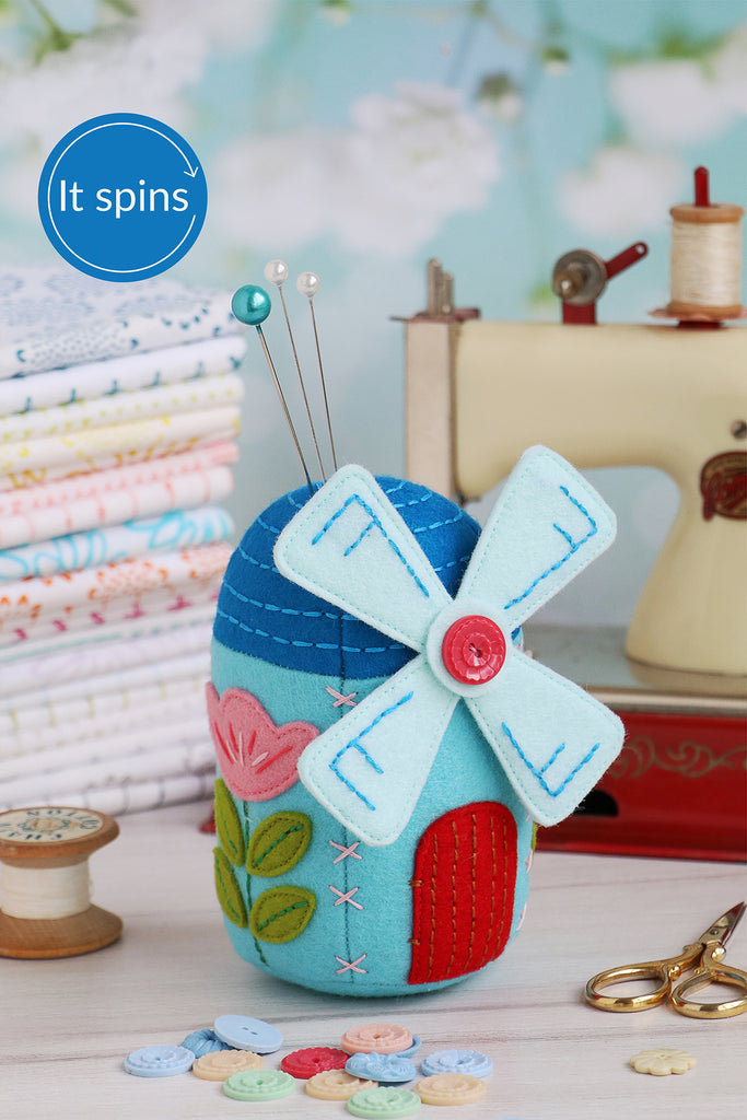 Decorative pin cushion shaped like a windmill with sewing supplies in the background