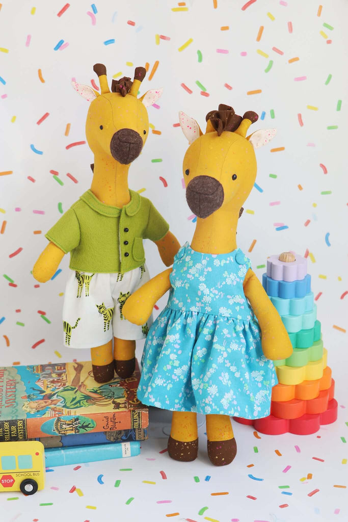 Noodle & Peach giraffe soft toys posed with rainbow blocks and vintage books on a sprinkle-themed backdrop.