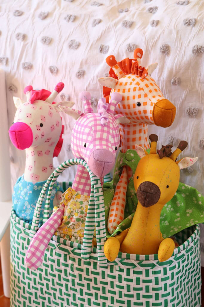 Group of colorful handmade giraffe dolls in a woven basket, showcasing vibrant fabrics and clothing styles.