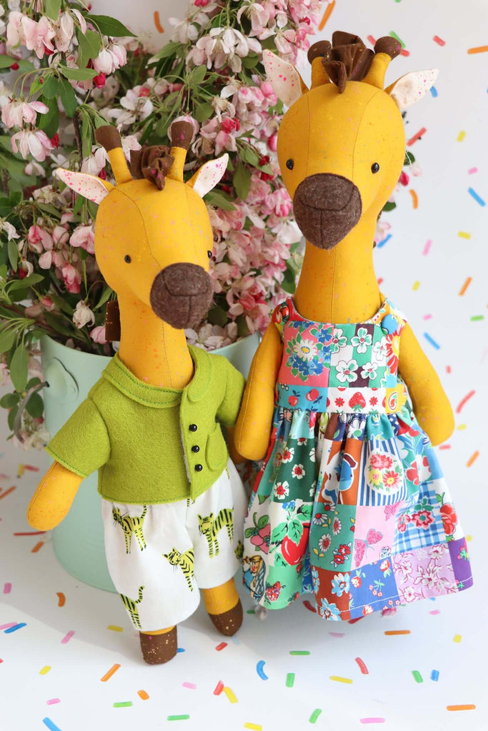 Pair of yellow handmade giraffe dolls in a patchwork dress and tiger shorts with a flower-filled background.