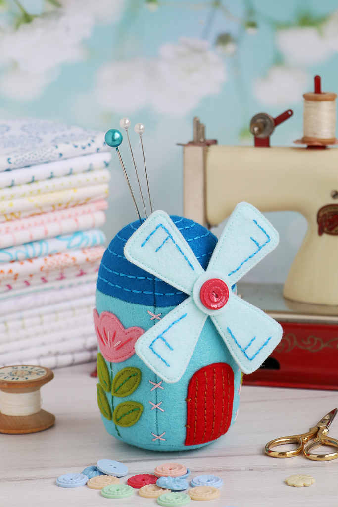 Colorful windmill-shaped pincushion with sewing tools on a table.
