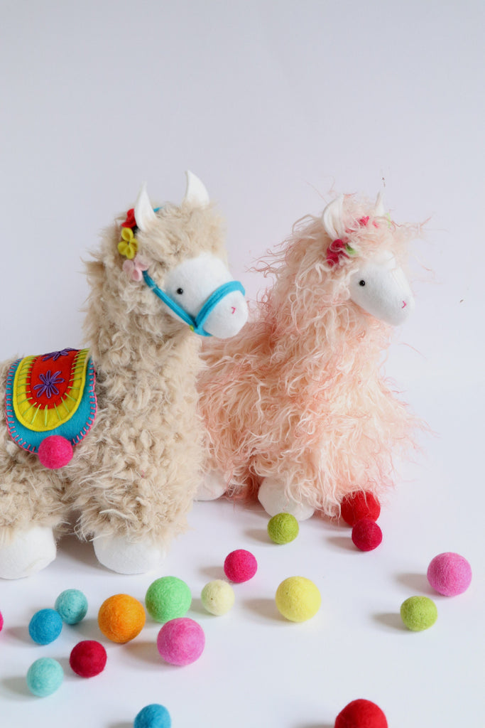 Handmade plush llama toys with curly fur, colorful felt saddle and garland, surrounded by bright felt balls. Soft toy sewing pattern example.