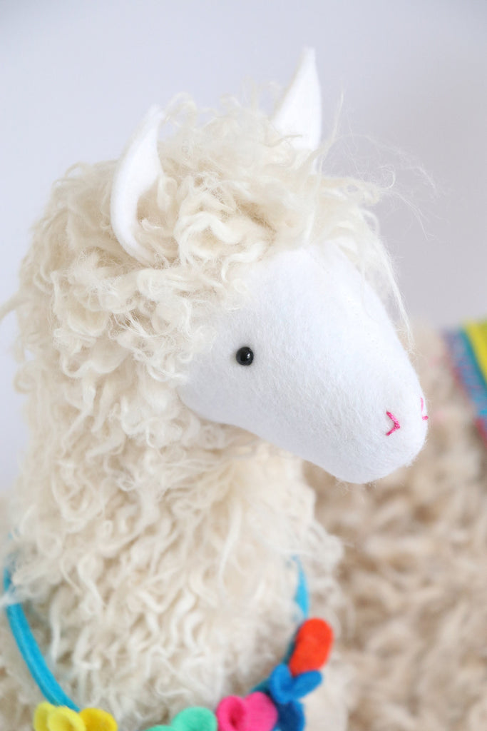 Curly plush llama soft toy with colorful felt flower garland necklace, made using a DIY sewing pattern from RicRac.